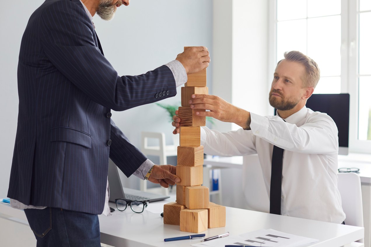 Serious Entrepreneurs of Different Ages Building Tower Together as Metaphor for Business Succession